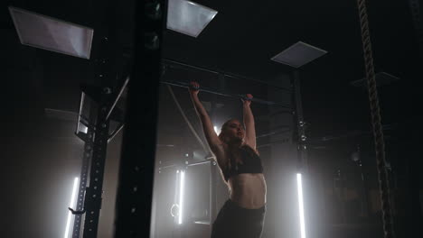 A-sporty-young-woman-pulls-herself-up-on-a-horizontal-bar-in-a-dark-gym-in-a-beautiful-neon-backlight.-Endurance-and-perseverance-in-pulling-up-movement-towards-the-goal